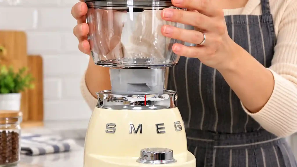 Hands seating a bean hopper onto a Smeg-style coffee grinder base.